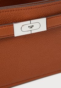 Smeđa kožna torba s teksturiranim završetkom, sadrži srebrno kopčanje i kontrastne šavove duž rubova.