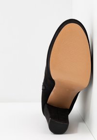 Czarna zamszowa szpilka z gładkim, ostrym noskiem i teksturowaną gumową podeszwą, prezentująca elegancki i prosty design.