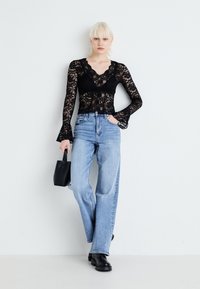 Top negru din dantelă cu mâneci lungi și decolteu în V, asociat cu blugi drepti cu talie înaltă, de culoare bleu deschis și botine negre masive.