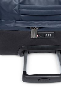 Maleta de tela azul oscuro con cierre de doble cremallera, cerradura de combinación y asa metálica retráctil. Base negra texturizada para mayor estabilidad.