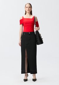 Bodysuit rojo sin mangas combinado con una falda maxi de mezclilla negra con una abertura frontal, acompañado de un bolso negro de hombro y tacones de punta.