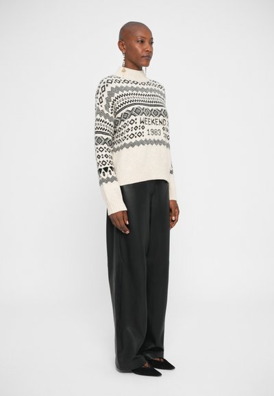 Pulover tricotat în crem cu modele geometrice negre și textul "WEEKEND 1983"; asortat cu pantaloni evazați negri și balerini cu vârf ascuțit.