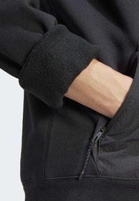 Svart sweatshirt med en texturerad fleecekrage och en funktionell dragkedjeficka med ett kontrasterande tyg inuti.