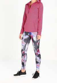 Felpa con zip rosa dal tessuto texturizzato, abbinata a leggings aderenti con un motivo astratto colorato in nero, rosa e grigio. Scarpe da ginnastica nere.