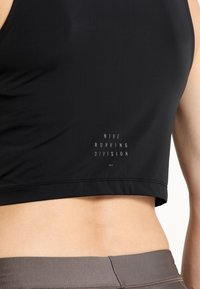Gros plan d'une personne portant un crop top noir Nike Running Division et des leggings de sport gris, montrant le ventre et la taille haute.