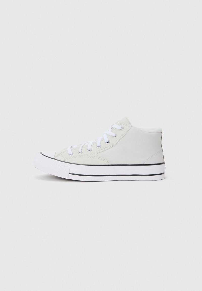 Baskets montantes blanches avec des lacets blancs, une bordure noire sur la semelle et une semelle en caoutchouc plate sur un fond clair uni.