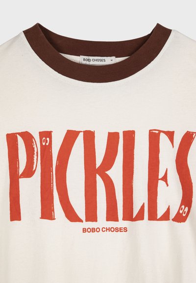 Biele tričko s hnedým golierom, na ktorom je veľký oranžový nápis "PICKLES" s očami a menším nápisom značky "BOBO CHOSES" pod ním.