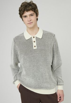 Pull en maille avec motif pied-de-poule en noir et crème. Il présente un col, trois boutons marron, et des poignets et un ourlet côtelés.