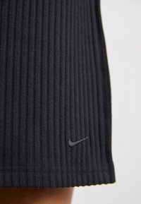 Svart ribbad kjol i tyg, med en subtil Nike-logotyp vid fållen. Texturerad yta med växlande upphöjda och plana ränder.