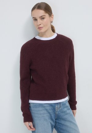 Maglione a maglia bordeaux con finitura testurizzata, collo rotondo e maniche lunghe, indossato sopra una camicia bianca, abbinato a jeans blu.