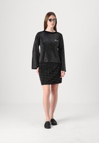 Svarte bluser med lange ermer prydet med reflekterende nagler, kombinert med en tettsittende svart skjørt med sølvfargede nagler. Brukt med svarte sko.