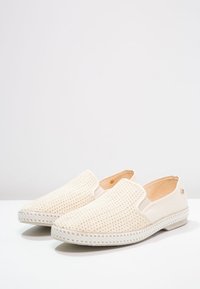 Beige instap schoenen met geweven textuur, leren zijkanten en rubberen zool. Bevat een witte stikaccent langs de zool en een klein logo detail.
