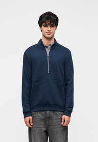 Πουλόβερ μπλε ναυτικό με ψηλό γιακά, φερμουάρ στη μέση μπροστά και υφασμάτινη κάτω επιφάνεια με υφή. Διαθέτει μπροστινή τσέπη και ριμπ μανσέτες.