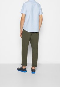 Camicia azzurro chiaro a maniche corte, pantaloni verde oliva e scarpe nere con suole blu. I pantaloni sono arrotolati all'orlo per un tocco di dettaglio.