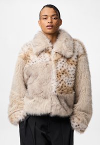 Kurtka z sztucznego futra w beżowych tonach, charakteryzująca się puszystą fakturą, dużym kołnierzem oraz wzorem patchworkowym z cętkowanymi akcentami.