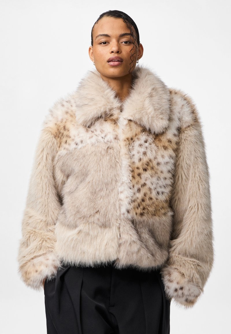 Kurtka z sztucznego futra w beżowych tonach, charakteryzująca się puszystą fakturą, dużym kołnierzem oraz wzorem patchworkowym z cętkowanymi akcentami.