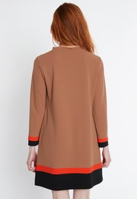 Braunes Kleid mit langen Ärmeln, das am Saum und an den Bündchen rot-schwarze Streifenakzente aufweist, aus glattem Stoff gefertigt und mit einem schlichten runden Halsauschnitt.