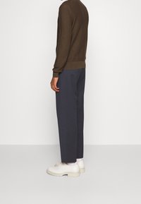 Brunstickad tröja, marinblå byxor och beiga skor. Tröjan har ribbade mudd och nederkant; skorna har en tjock sula.