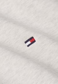 Primo piano di tessuto beige con un piccolo logo ricamato che presenta strisce orizzontali in blu navy, bianco e rosso.