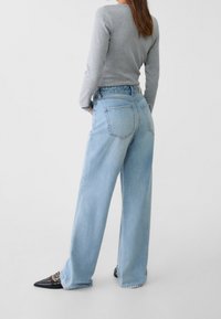 Ljust blå vida jeans med hög midja, med två bakfickor och fransat avslut, matchade med en grå långärmad topp och svarta klackar.