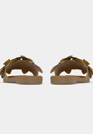 Par brune flade slid-sandaler med blomsterapplikationer set bagfra mod en ensfarvet baggrund.