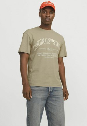 Olijfgroene katoenen t-shirt met ronde hals, korte mouwen en witte bedrukte tekst. Gekoppeld aan lichtblauwe denim jeans.