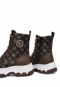 Stivali alti marroni e neri con loghi a motivo, suole spesse bianche, cerniera laterale su un stivale e dettagli con lacci sul davanti.