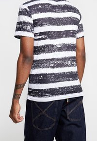 Pruhované černobílé tričko s texturovaným vzorem. Krátké rukávy, kulatý výstřih, spárováno s tmavými džíny s kontrastním šitím.