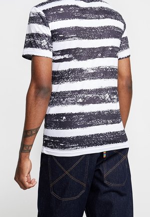 Camiseta a rayas blancas y negras con un patrón texturizado. Mangas cortas, cuello redondo, combinada con unos vaqueros de mezclilla oscuros con costuras en contraste.