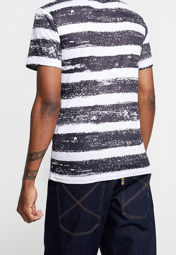 Pruhované černobílé tričko s texturovaným vzorem. Krátké rukávy, kulatý výstřih, spárováno s tmavými džíny s kontrastním šitím.