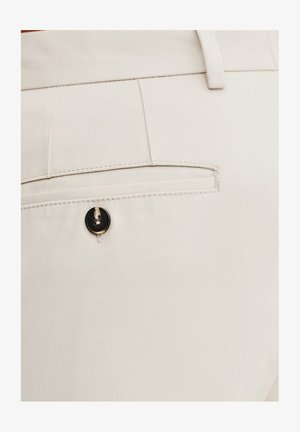 Jasnekremowe spodnie o gładkiej fakturze, z tylną kieszenią zapiętą czarnym guzikiem i subtelnym detalem przeszycia.