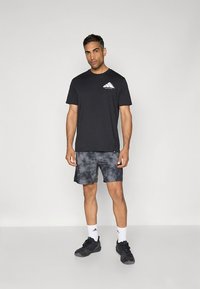 Must t-särk valge logoga rinnal, kombineeritud tume tie-dye lühikestega. Kandmisel mustad spordijalatsid ja valged sokid.