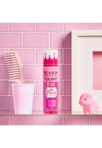 Revlon Equave Kids utredende balsam i en rosa flaske med krone-design, ved siden av en rosa kam, rosa kopp og en rosa svinefigur på en rosa flislagt bakgrunn.