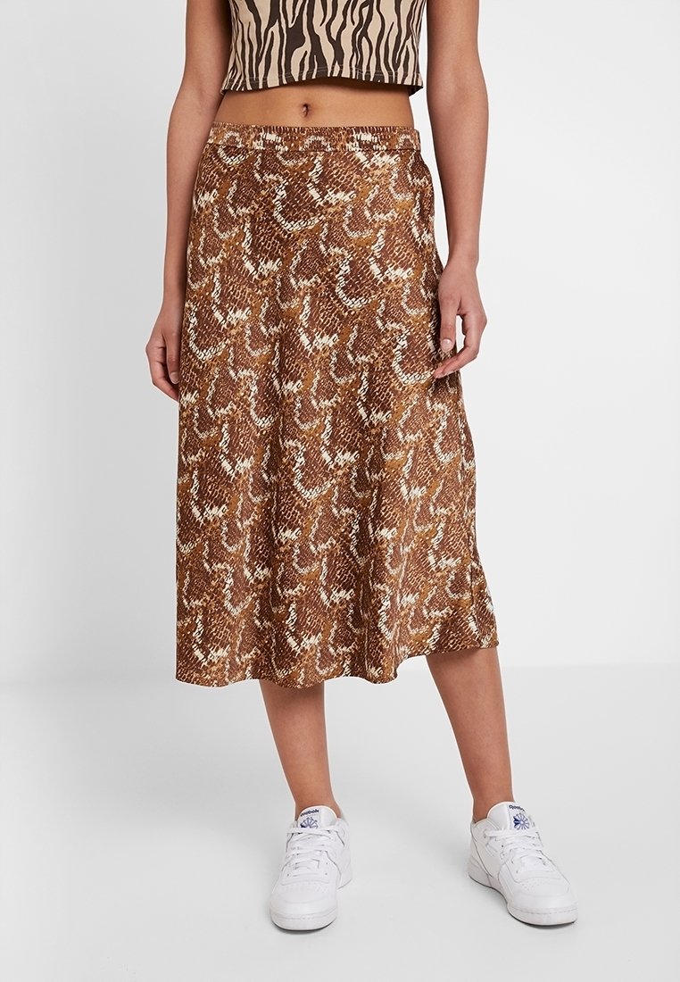 Brun ormtryckt kjol i lättviktig tyg, med en svävande design och längd till midjan, kombinerad med vita sneakers.