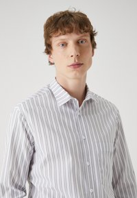 Striped button-up shirt in white and gray. Features a classic collar, chest pocket, and textured fabric with vertical stripes.