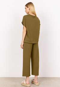 Outfit coordinato in verde oliva composto da una maglietta corta a maniche corte con colletto rotondo e pantaloni a gamba larga. Tessuto morbido con design minimalista.