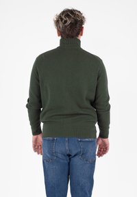Groene gebreide trui met een hoge kraag, geribbelde manchetten en zoom. Draagt het met blauwe jeans, toont de achterkant van het geheel.