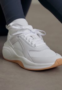 Białe buty sportowe z siateczkowymi detalami, zaokrąglonym noskiem i wyściełaną podeszwą. Posiada cienkie sznurowadła i brązową gumową podeszwę.