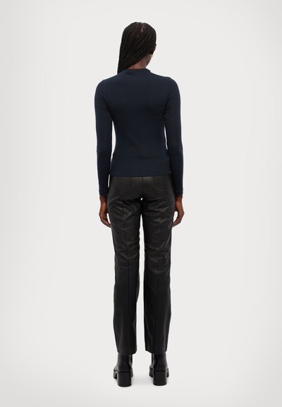 Marine langærmet top kombineret med høj talje sort læderbukser, der har en tætsiddende silhuet og glat tekstur. Kraftige sorte støvler fuldender looket.