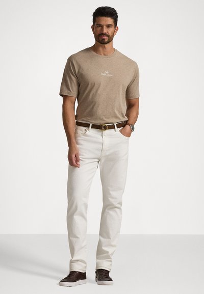 T-shirt pour homme à manches courtes, de couleur marron clair avec logo, associé à un jean blanc et des baskets marron foncé. Offre une coupe classique et un look décontracté.