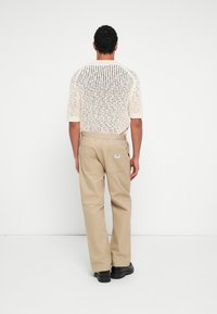 Kremowy sweter z krótkim rękawem wykonany na drutach z otwartym wzorem, w połączeniu z beżowymi spodniami; oba w luźnym kroju. Miękka tkanina, subtelne detale szwów.