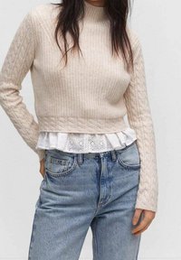 Pull crème à côtes avec détail en tricot torsadé, superposé sur un top péplum en broderie anglaise blanche, assorti à un jean taille haute bleu clair.