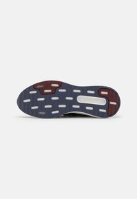 Sportssko såle med en mørkeblå bunn og røde og hvite aksenter, ventilasjonshull og teksturert gummi for grep.