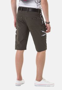 Khaki Cargo-Shorts mit mehreren Taschen, verstärkter Naht und schwarzen Logo-Akzenten an den Seiten, mit geradem Schnitt und strukturiertem Stoff.