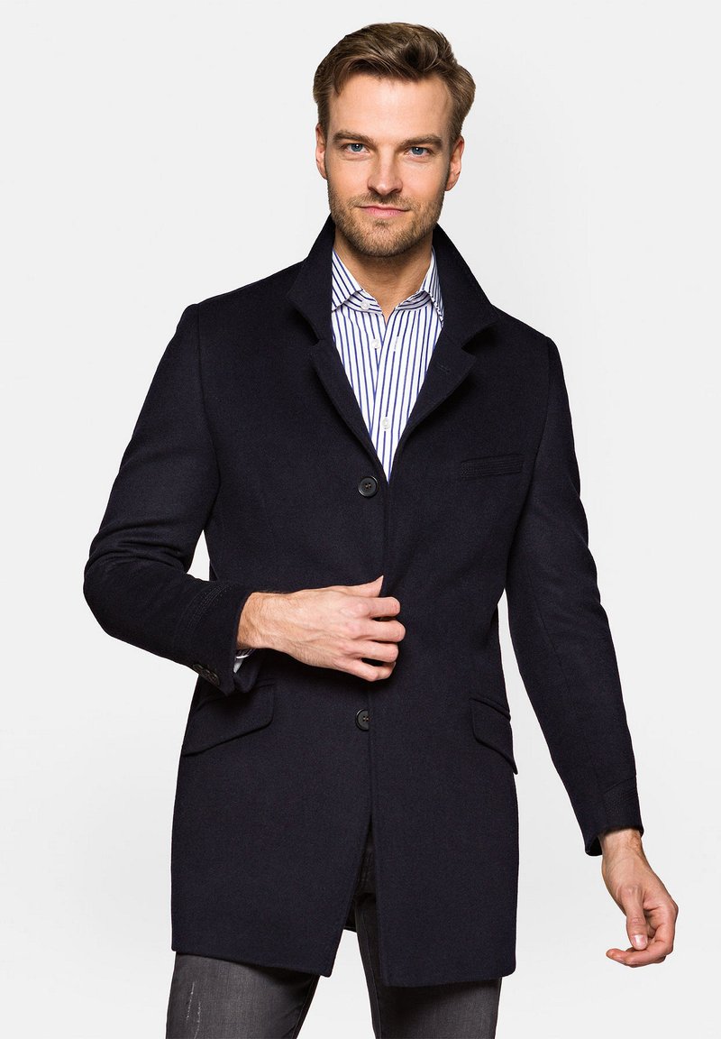 Granatowy płaszcz z wełny z domieszką włókien syntetycznych, z kołnierzem typu notch, dwiema przednimi kieszeniami oraz zapięciem na guziki. Płaszcz jest dopasowany w prostej sylwetce.