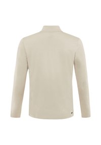 Top beige de manga larga con cuello alto, visto desde atrás, con una pequeña etiqueta negra cerca del dobladillo inferior sobre un fondo blanco.