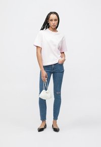 Rózsaszín rövid ujjú pamut póló, hozzá párosítva kék, szakadt térdű szűk farmernadrág. Kiegészítők: fehér húzózsinóros táska és fekete balerinacipő.