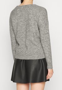 Grå, stickad tröja med långa ärmar, i kombination med en svart, fusk läderkjol. Mjuk textur och avslappnad passform, med en rundad halsringning.