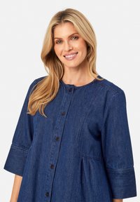 Abito in denim blu scuro con scollatura rotonda, maniche a tre quarti, chiusura frontale a bottoni e dettaglio arricciato in vita.
