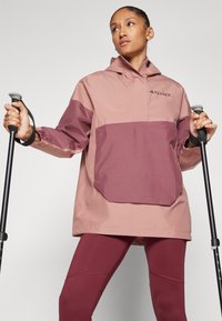 Kurtka softshell w odcieniach różu i burgunda, z dużą przednią kieszenią, elastycznymi mankietami i kapturem. W zestawie z kijkami trekkingowymi.